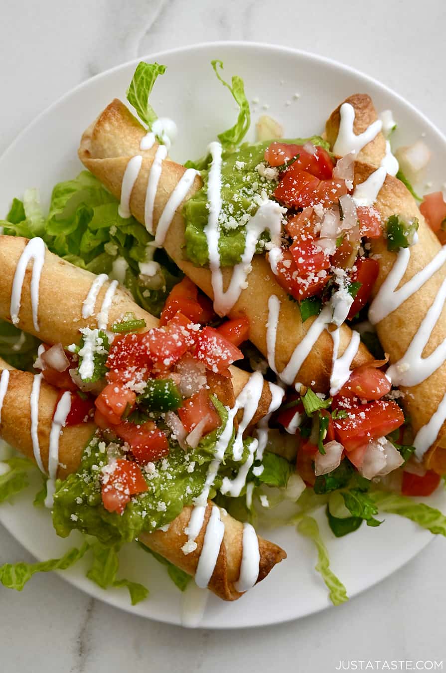 A top-down view of air fryer cheese taquitos topped with pico de gallo and guacamole on a white plate atop a bed of lettuce