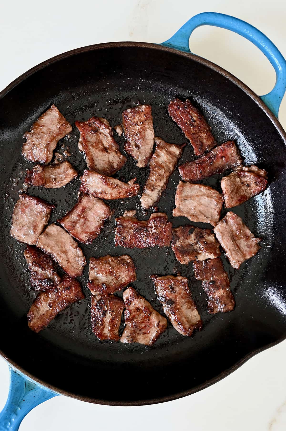 Seared flank steak pieces in a large skillet.