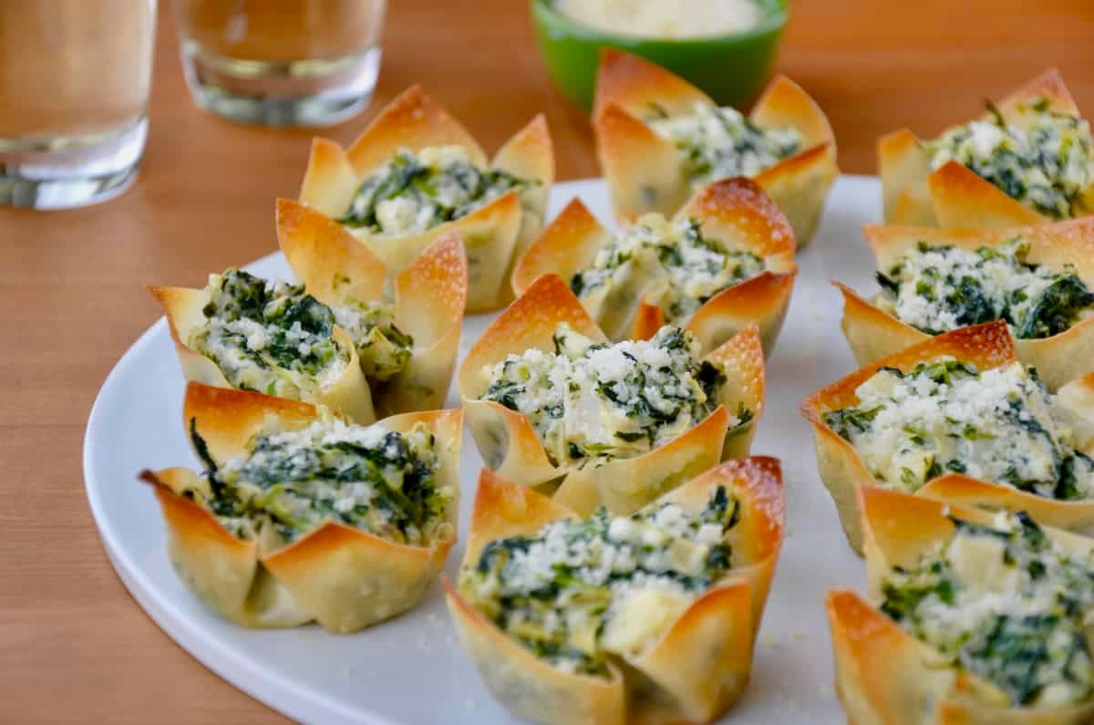 Creamy artichoke spinach dip inside of a baked wonton cup on a white serving platter.