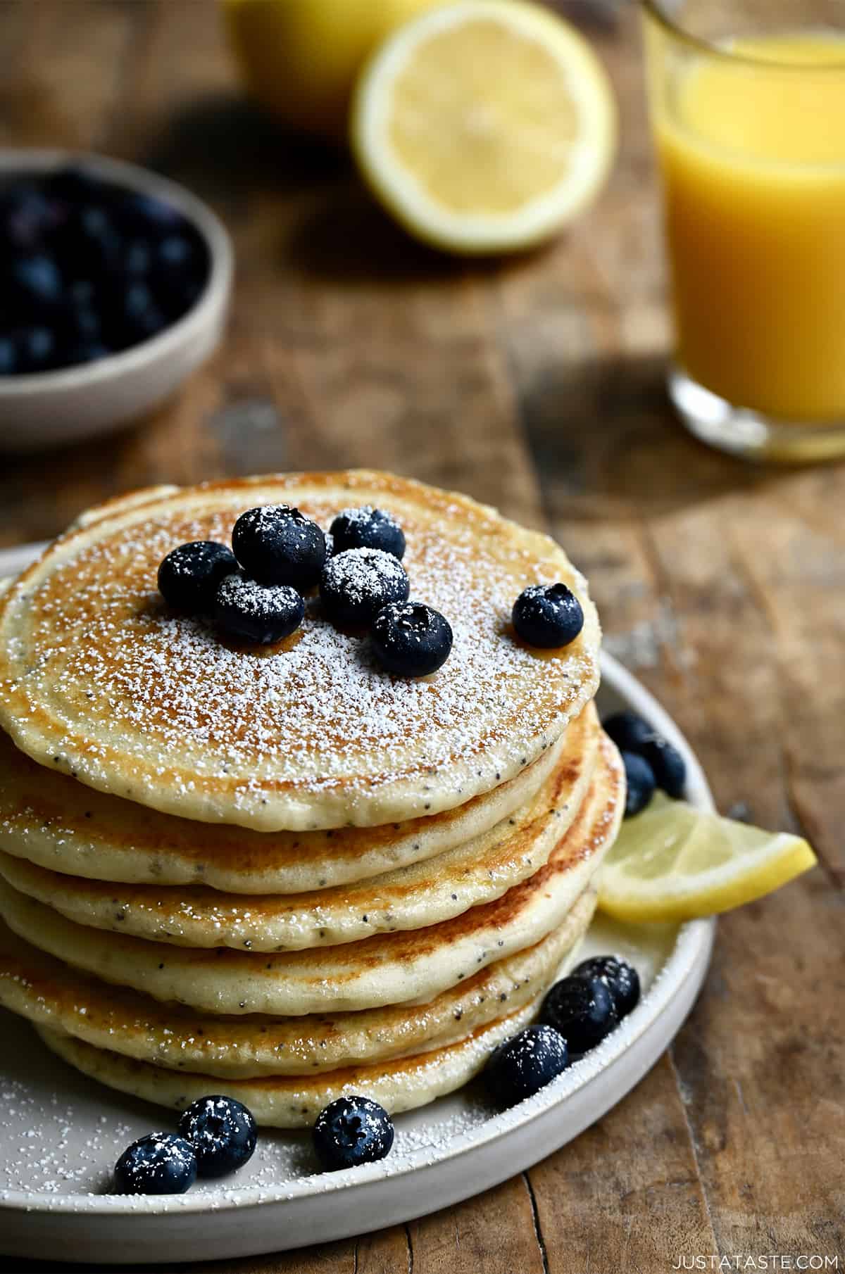A tall stack of lemon poppy seed pancakes topped with fresh blueberries and powdered sugar.