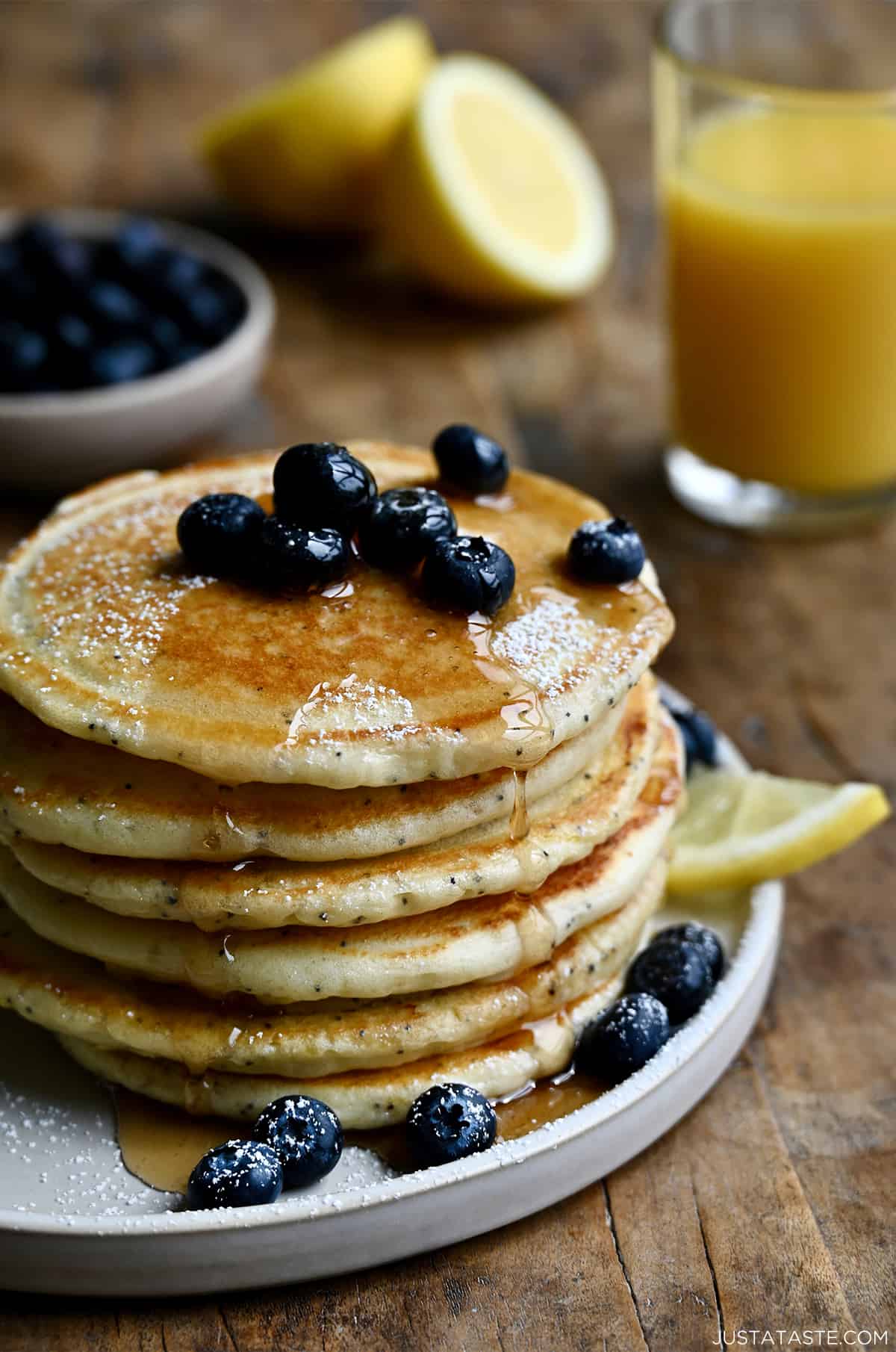A tall stack of lemon poppyseed pancakes topped with fresh blueberries and drizzled with maple syrup.