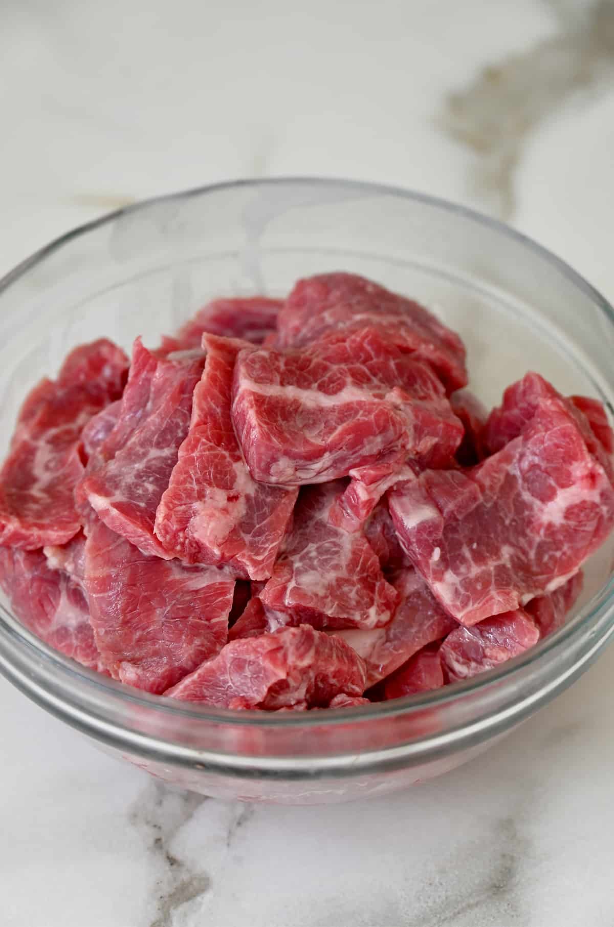 A clear bowl containing flank steak pieces in a cornstarch marinade.