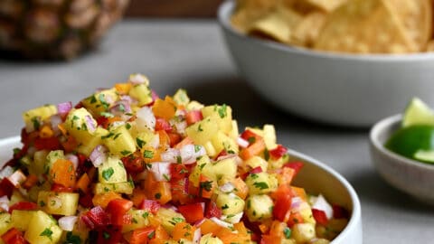 A white bowl filled to the top with fresh pineapple salsa with a small bowl in the background filled with tortilla chips.