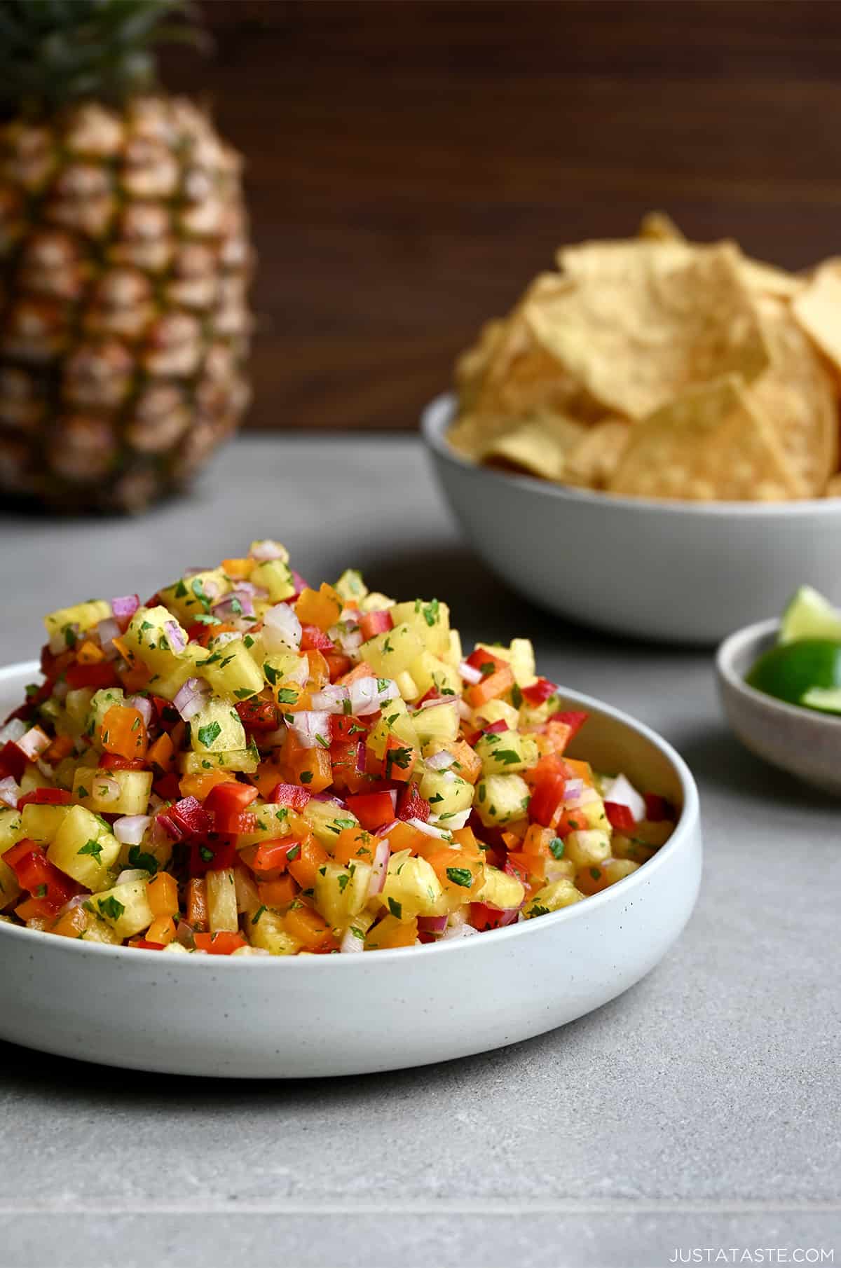 A white bowl filled to the top with fresh pineapple salsa with a small bowl in the background filled with tortilla chips.