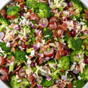 A top-down view of a large bowl containing broccoli grape salad with shredded mozzarella cheese and bacon crumbles.