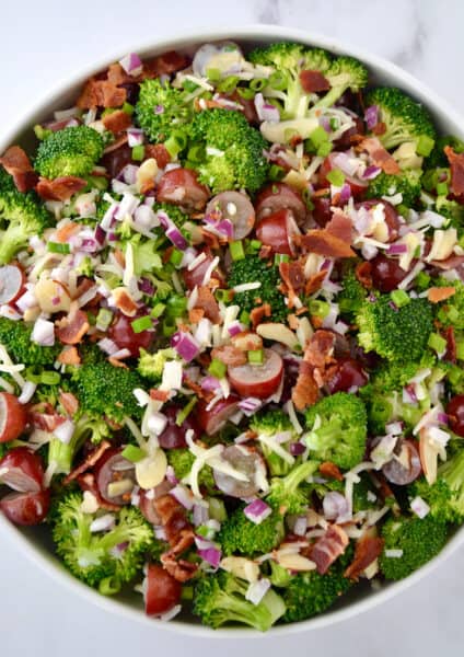 A top-down view of a large bowl containing broccoli grape salad with shredded mozzarella cheese and bacon crumbles.