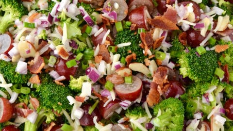 A top-down view of a large bowl containing broccoli grape salad with shredded mozzarella cheese and bacon crumbles.