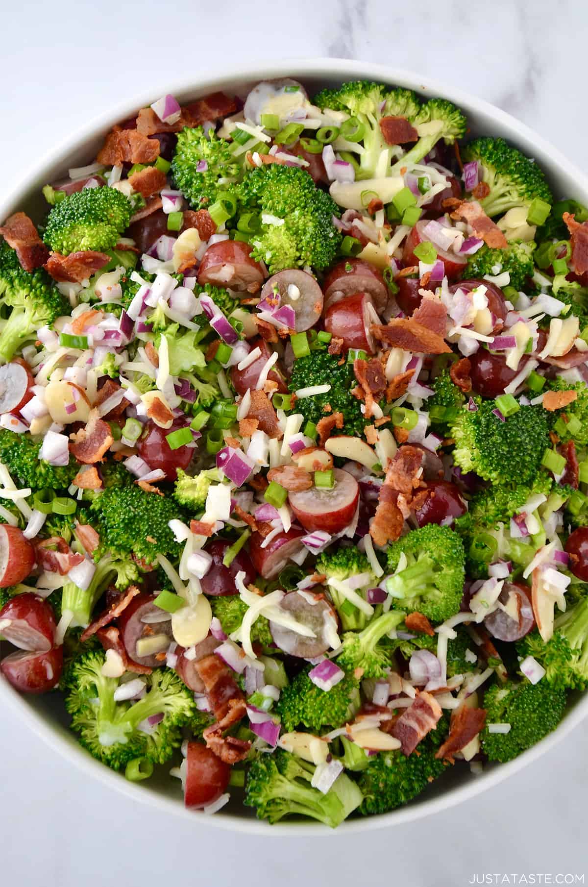 A top-down view of a large bowl containing broccoli grape salad with shredded mozzarella cheese and bacon crumbles.