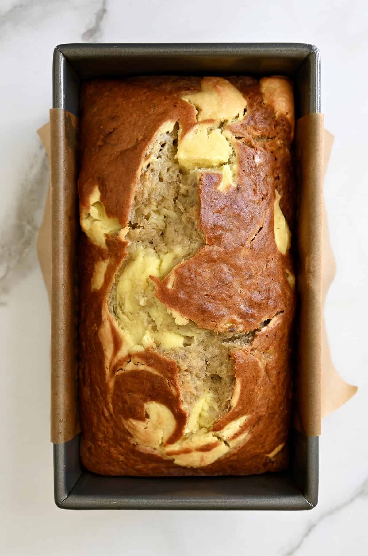 A loaf of banana cream cheese bread in a parchment paper-lined bread pan.