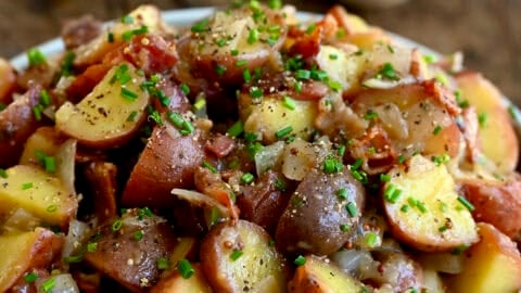 White serving bowl containing German potato salad with warm bacon dressing, bacon pieces and chopped fresh chives.