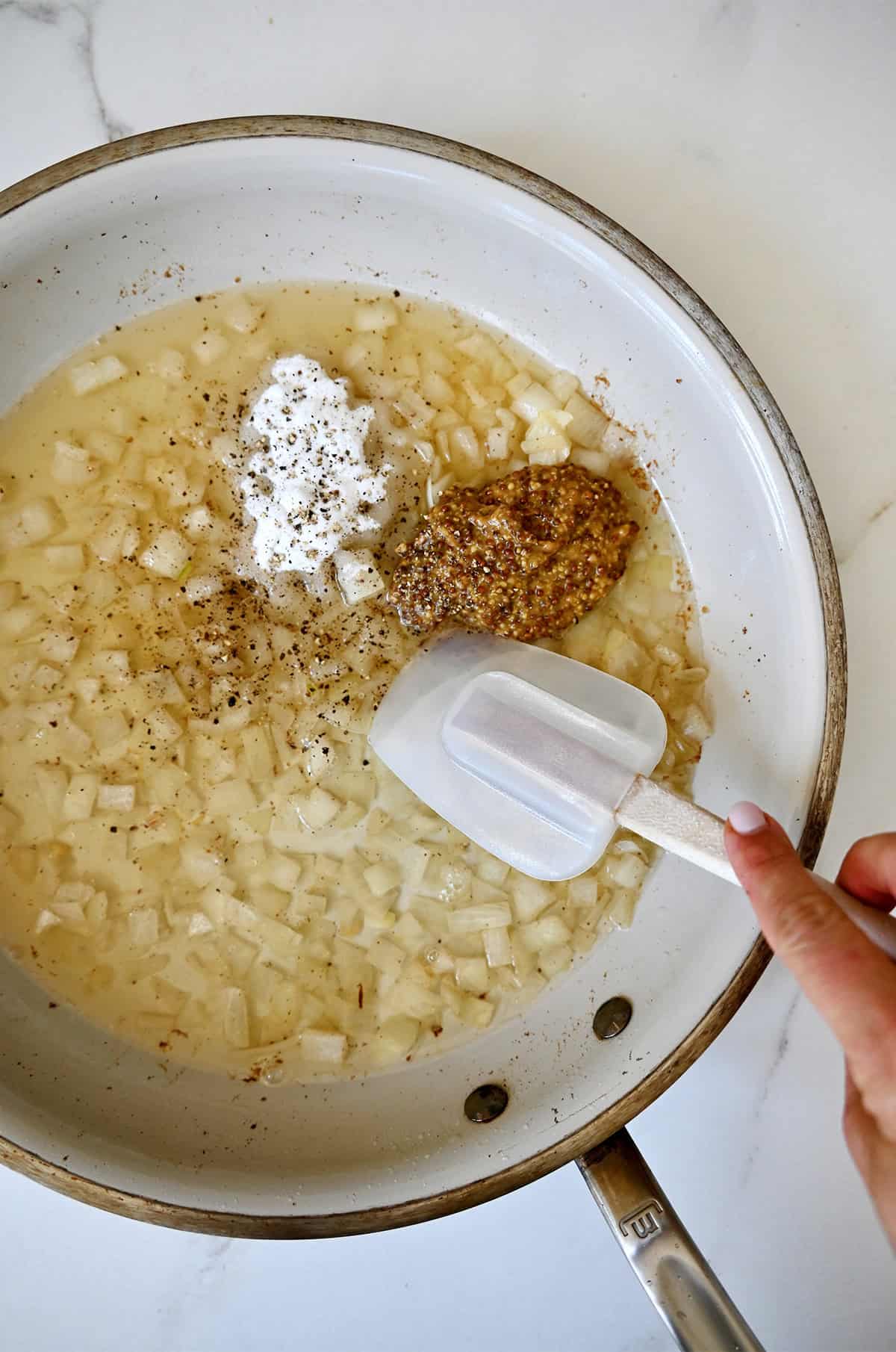 Adding whole grain mustard and sugar to a skillet with sautéed onions to make a bacon dressing.