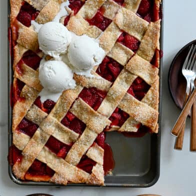 A top-down view of a Simple Strawberry Slab Pie topped with three scoops of vanilla bean ice cream and a corner piece cut out and on a plate next to it