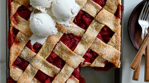 A top-down view of a Simple Strawberry Slab Pie topped with three scoops of vanilla bean ice cream and a corner piece cut out and on a plate next to it