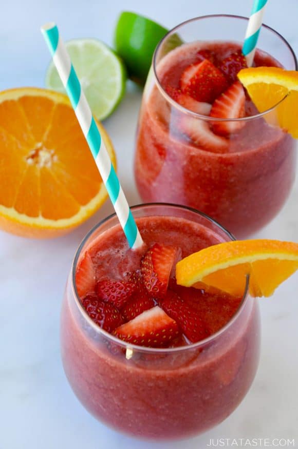 The Best Frozen Sangria topped with fresh strawberries served with an orange slice and straw