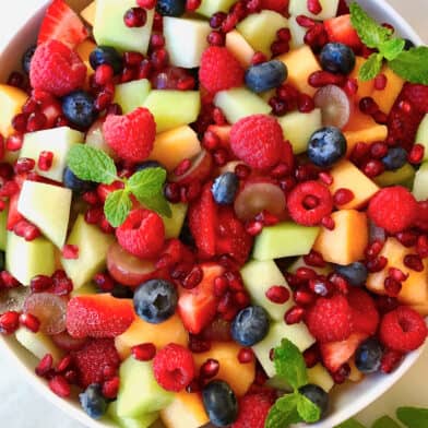 A large serving bowl containing fruit salad with diced cantaloupe and honeydew melon, blueberries, raspberries and pomegranate arils.