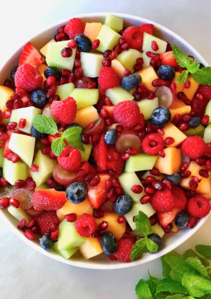 A large serving bowl containing fruit salad with diced cantaloupe and honeydew melon, blueberries, raspberries and pomegranate arils.