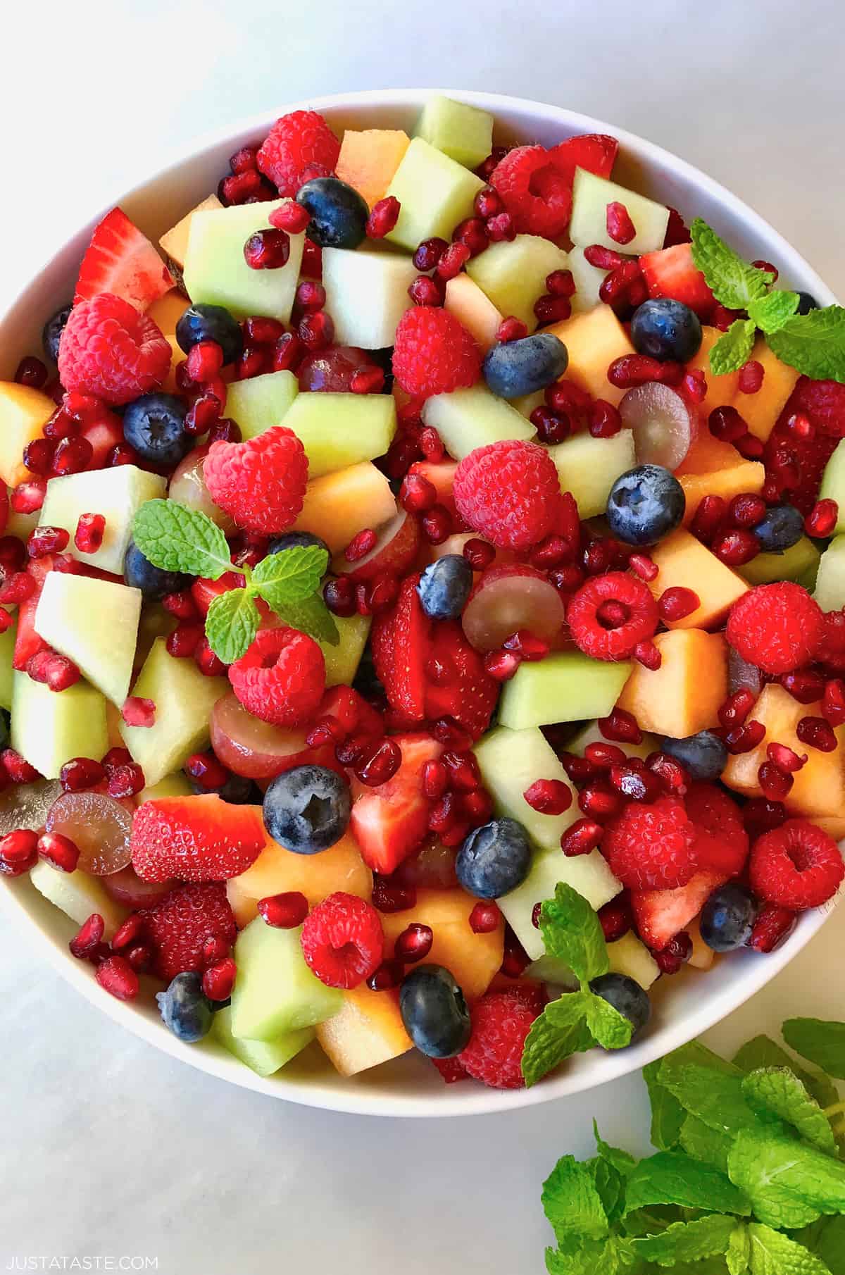 A large serving bowl containing fruit salad with diced cantaloupe and honeydew melon, blueberries, raspberries and pomegranate arils.