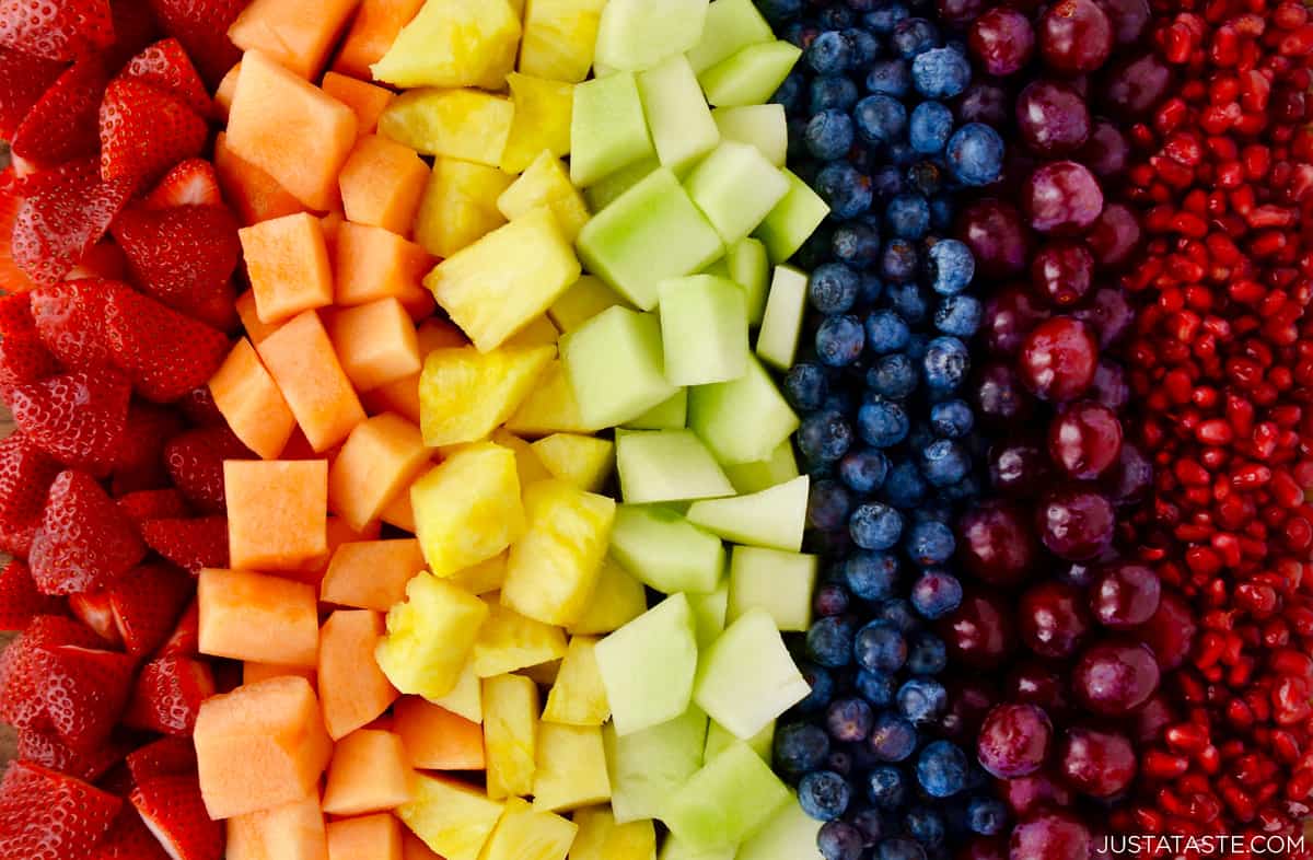 A rainbow of fresh fruit, including sliced strawberries, sliced cantaloupe, sliced pineapple, sliced honeydew melon, blueberries, purple grapes and pomegranate seeds.