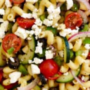 A closeup view of Greek Pasta Salad with Red Wine Vinaigrette that's loaded with sliced cucumbers, halved cherry tomatoes, sliced red onion, black olives and crumbled feta cheese.