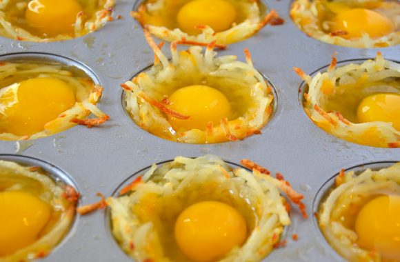 Cheesy hash brown cups in muffin tin with uncooked egg in center of each