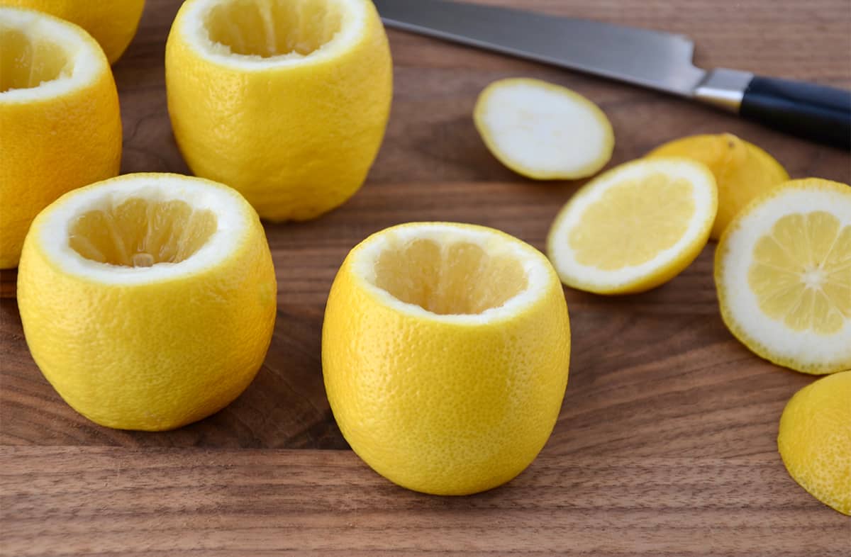 Hollowed out lemons on a wood surface next to a sharp knife.