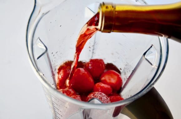 Wine being poured into blender with frozen strawberries