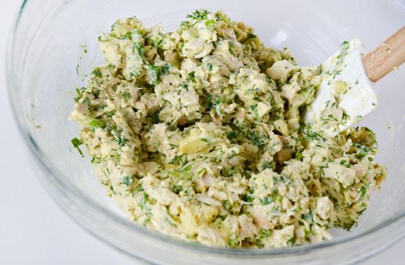 Mixed avocado chicken salad in clear bowl with spatula