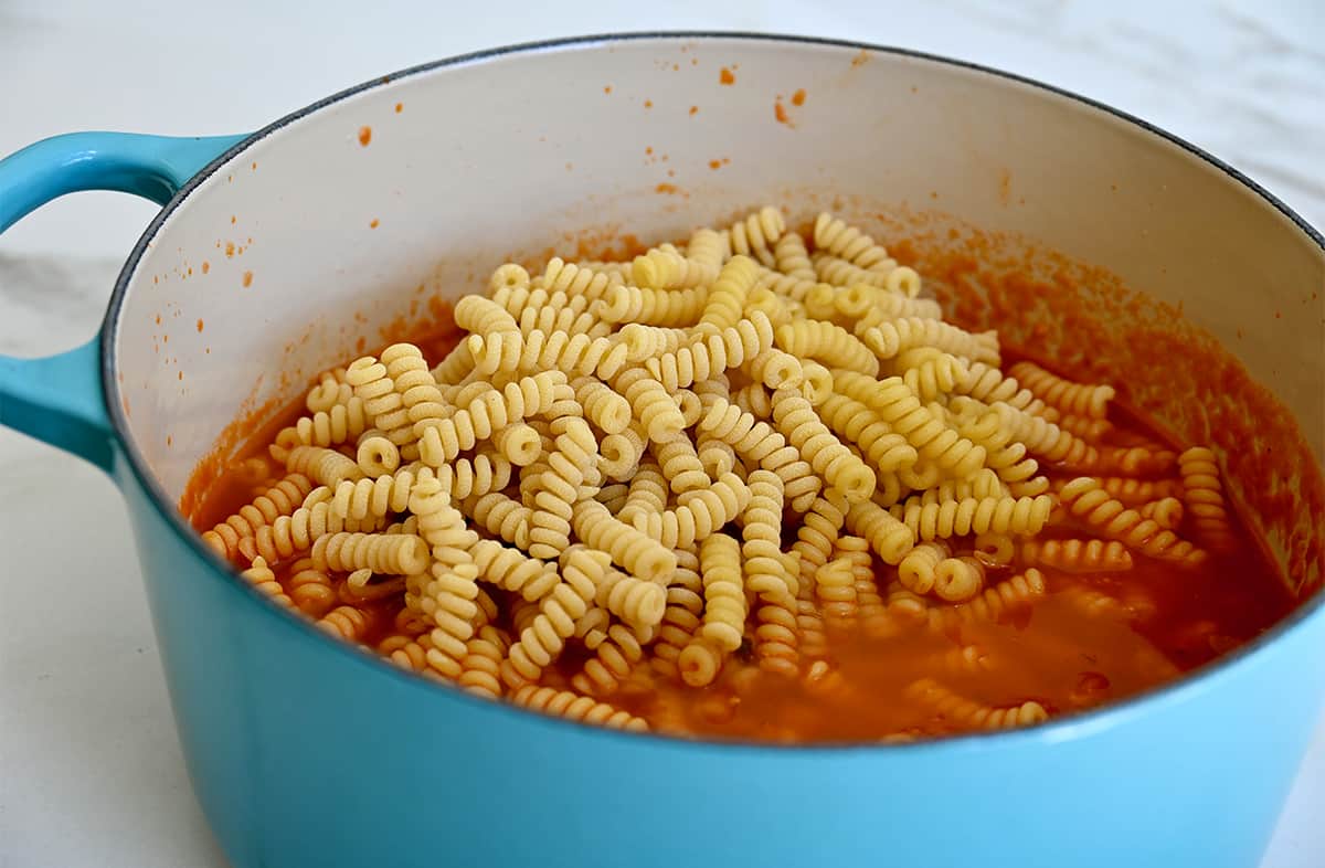 Noodles atop a meat marinara sauce in a large stockpot.