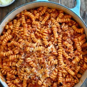 Pasta with marinara sauce and Italian sausage garnished with grated Parmesan cheese in a large stockpot.