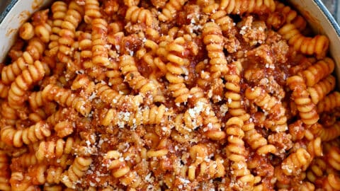 Pasta with marinara sauce and Italian sausage garnished with grated Parmesan cheese in a large stockpot.