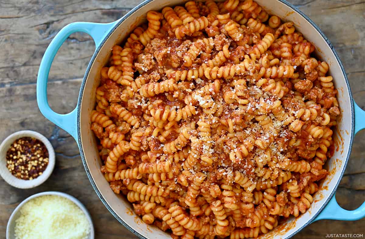 A large pot containing Italian sausage pasta coated in marinara sauce and garnished with Parmesan cheese.