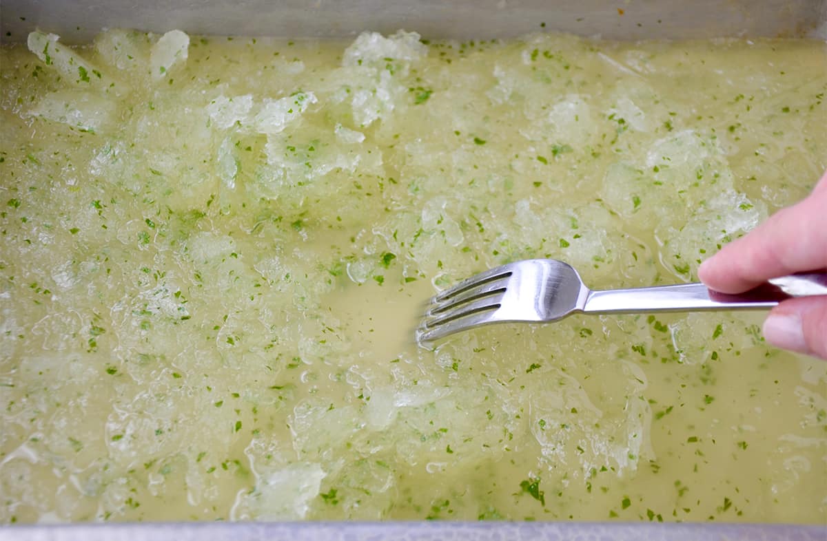 A fork scrapes partially frozen granita on a baking sheet.