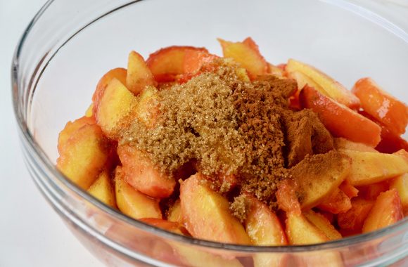 Sliced peaches with brown sugar and cinnamon in clear bowl