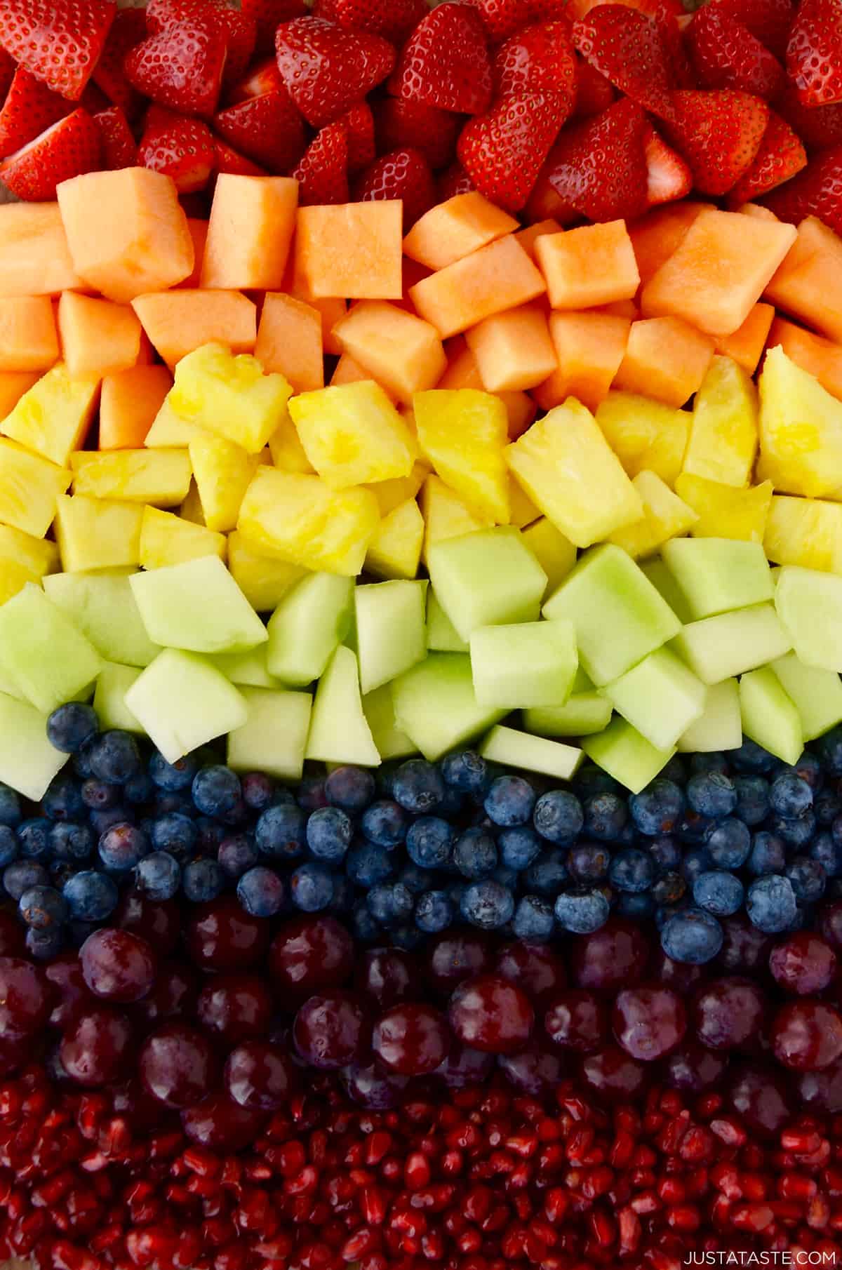 A rainbow of fresh fruit, including sliced strawberries, sliced cantaloupe, sliced pineapple, sliced honeydew melon, blueberries, purple grapes and pomegranate arils.