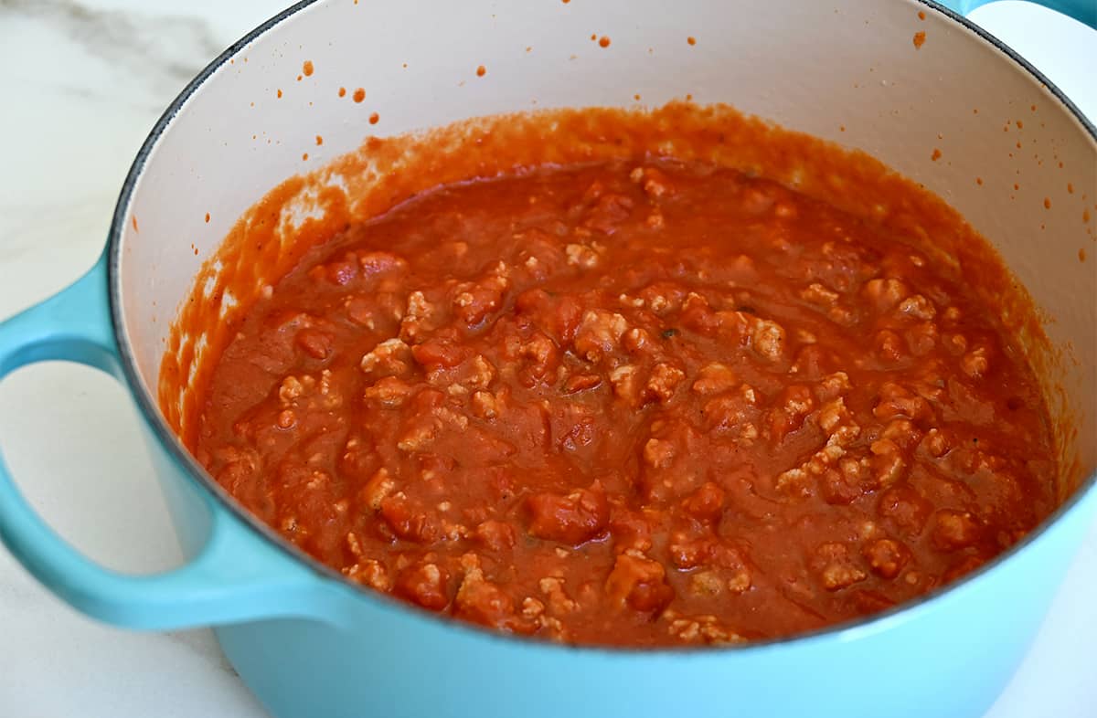 A large stockpot containing marinara sauce with sausage.