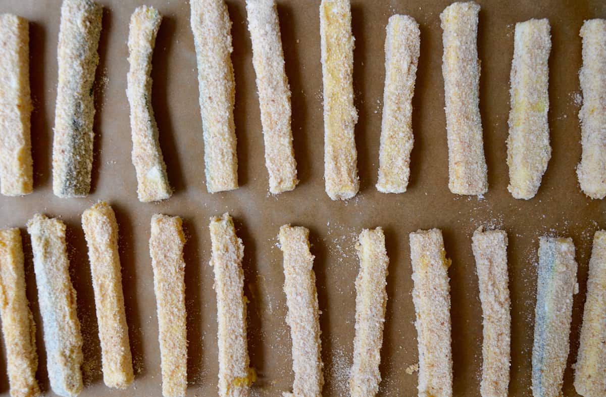 Two rows of battered zucchini fries atop parchment paper.