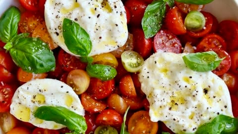 Burrata Caprese salad drizzled with olive oil in a large serving bowl.