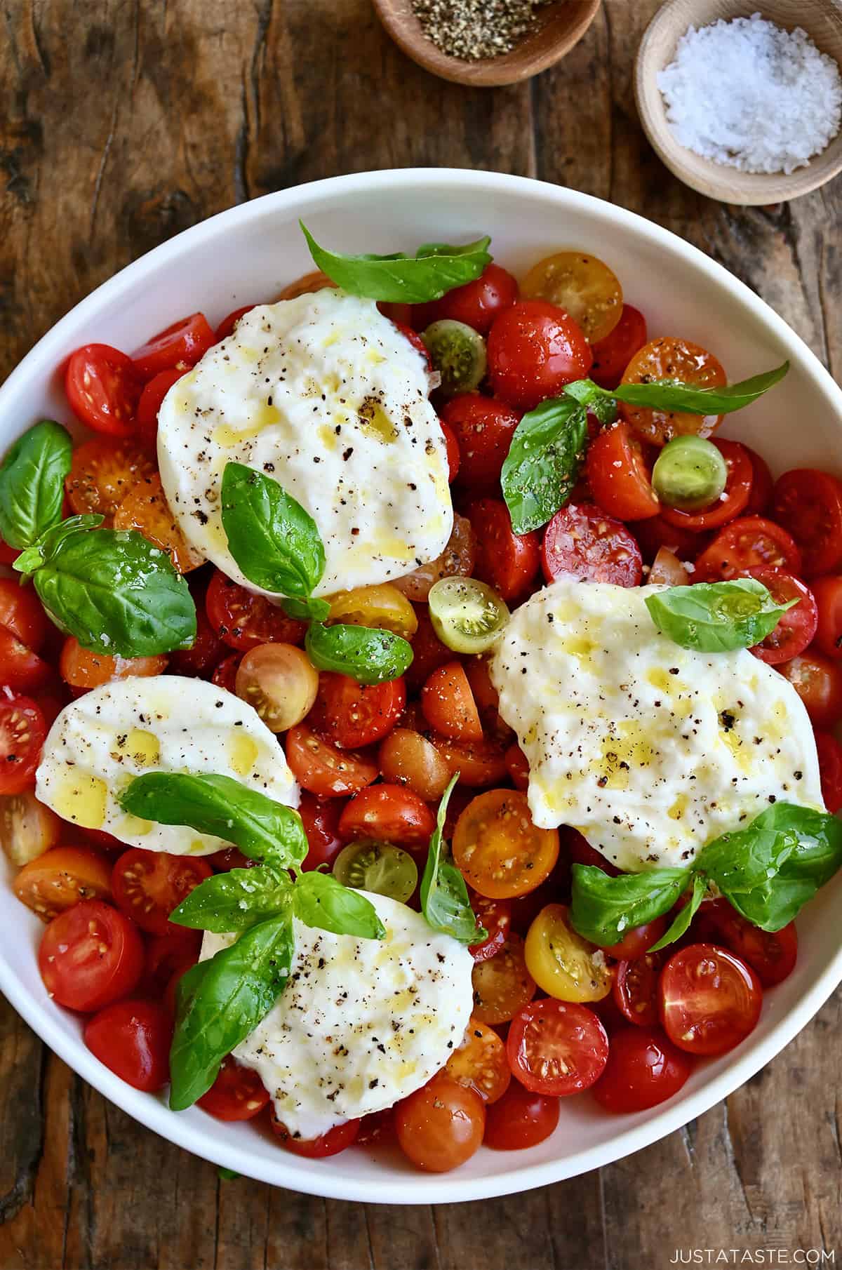 Burrata Caprese salad drizzled with olive oil in a large serving bowl.