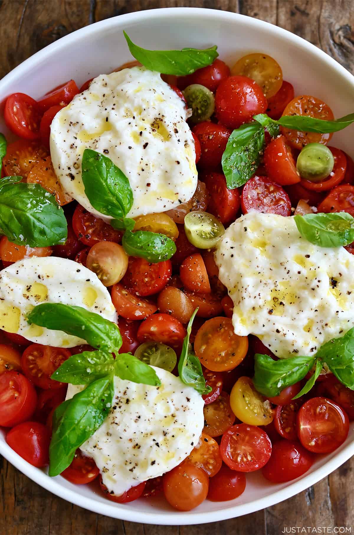 Caprese salad with burrata, freshly cracked pepper and large-flake sea salt drizzled with extra-virgin olive oil in a large serving bowl.