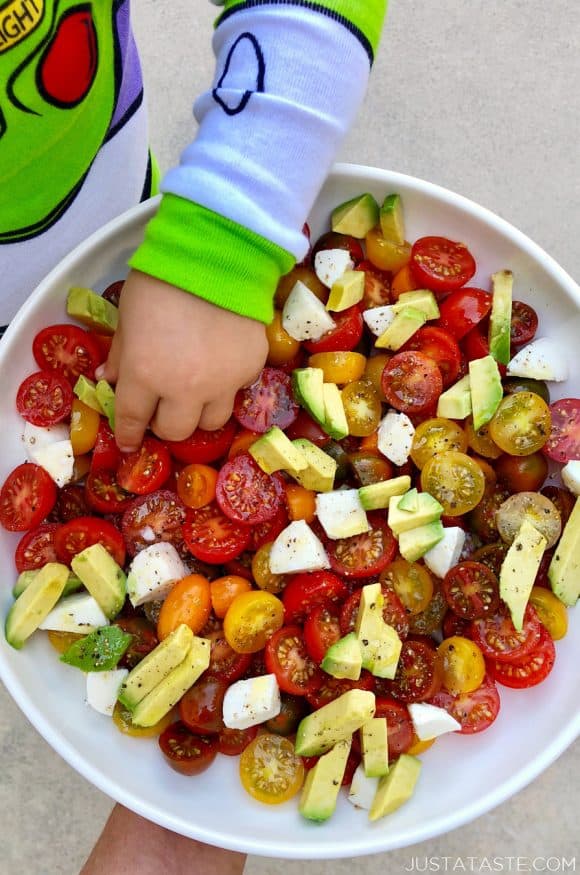 A white bowl containing cherry tomatoes and avocado with a little boy's hand reaching into it