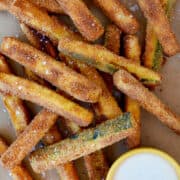 Top-down view of crispy baked zucchini fries topped with large-flake sea salt next to a small ramekin filled with ranch dressing.