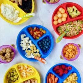 Various plates of kid food ideas with a child's hand reaching into one