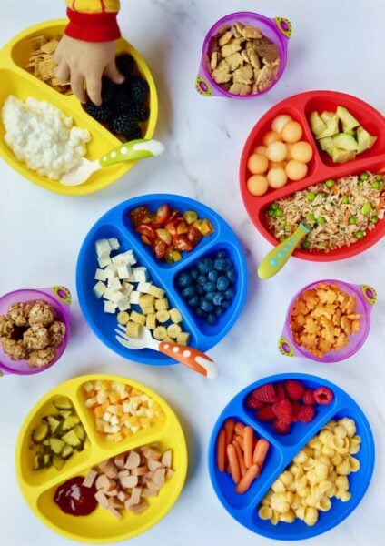Various plates of kid food ideas with a child's hand reaching into one