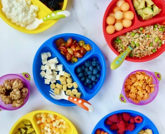 Various plates of kid food ideas with a child's hand reaching into one