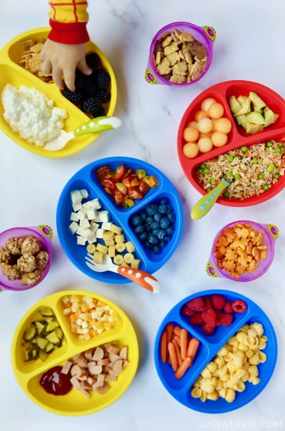 Various plates of kid food ideas with a child's hand reaching into one