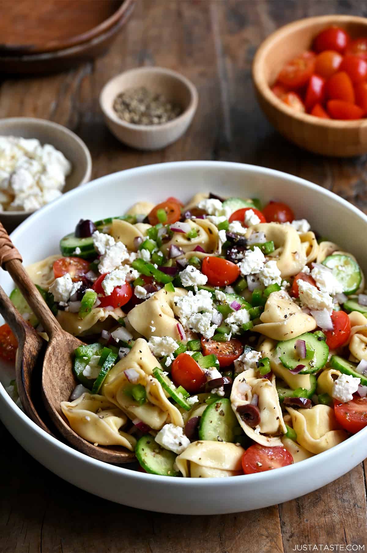 A large serving bowl containing pasta salad made with tortellini, cherry tomatoes, cucumber, Kalamata olives, feta cheese and green pepper.