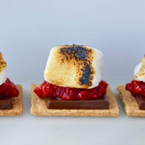 Three toasted marshmallows on graham crackers with fresh raspberries