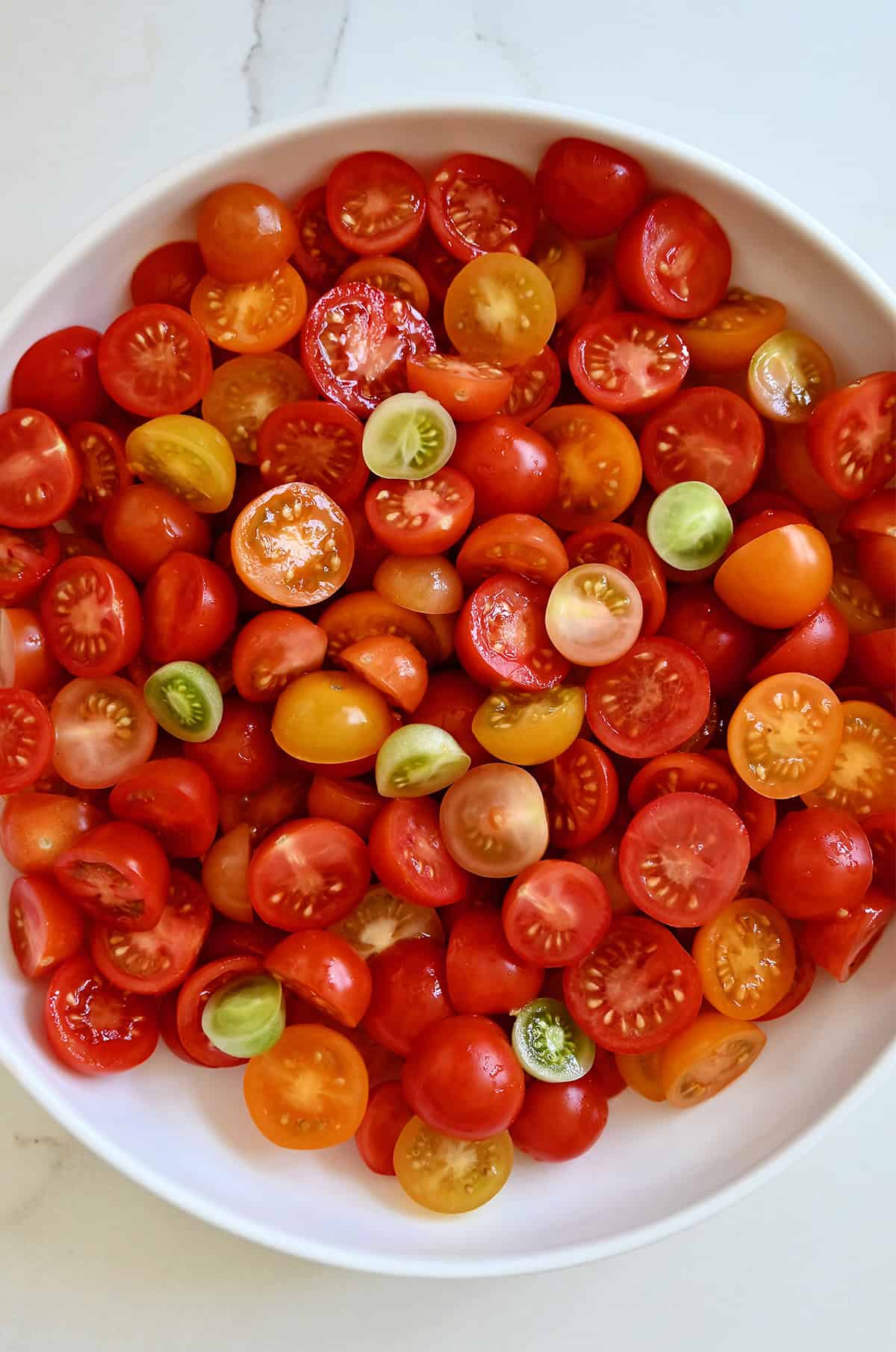 A large serving bowl filled with a rainbow of halved cherry tomatoes.