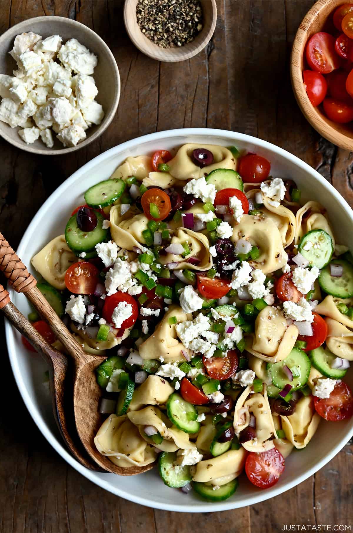 A large serving bowl containing Greek Tortellini Pasta Salad with olives, cherry tomatoes and feta cheese. 