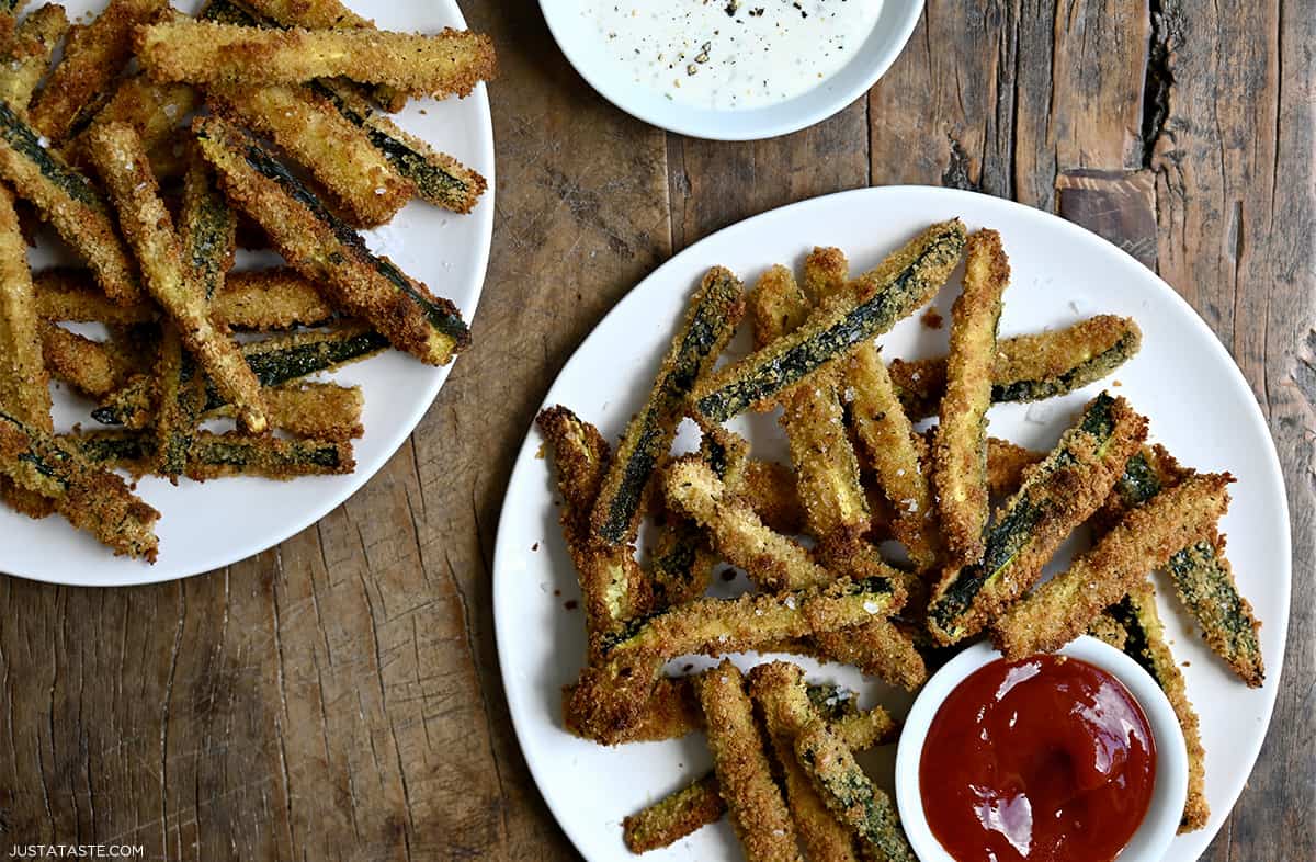 A white dinner plate piled high with crispy zucchini fries and a small bowl containing ketchup.